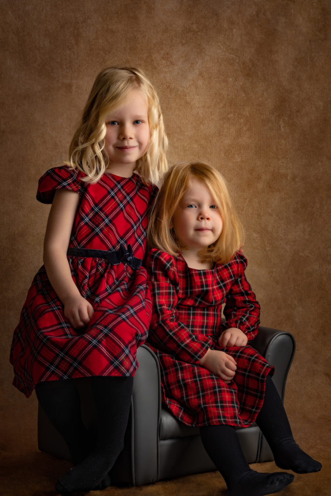 portrait fine-art de 2 sœurs habillées avec robe à carreaux rouge et noir assises dans un fauteuil