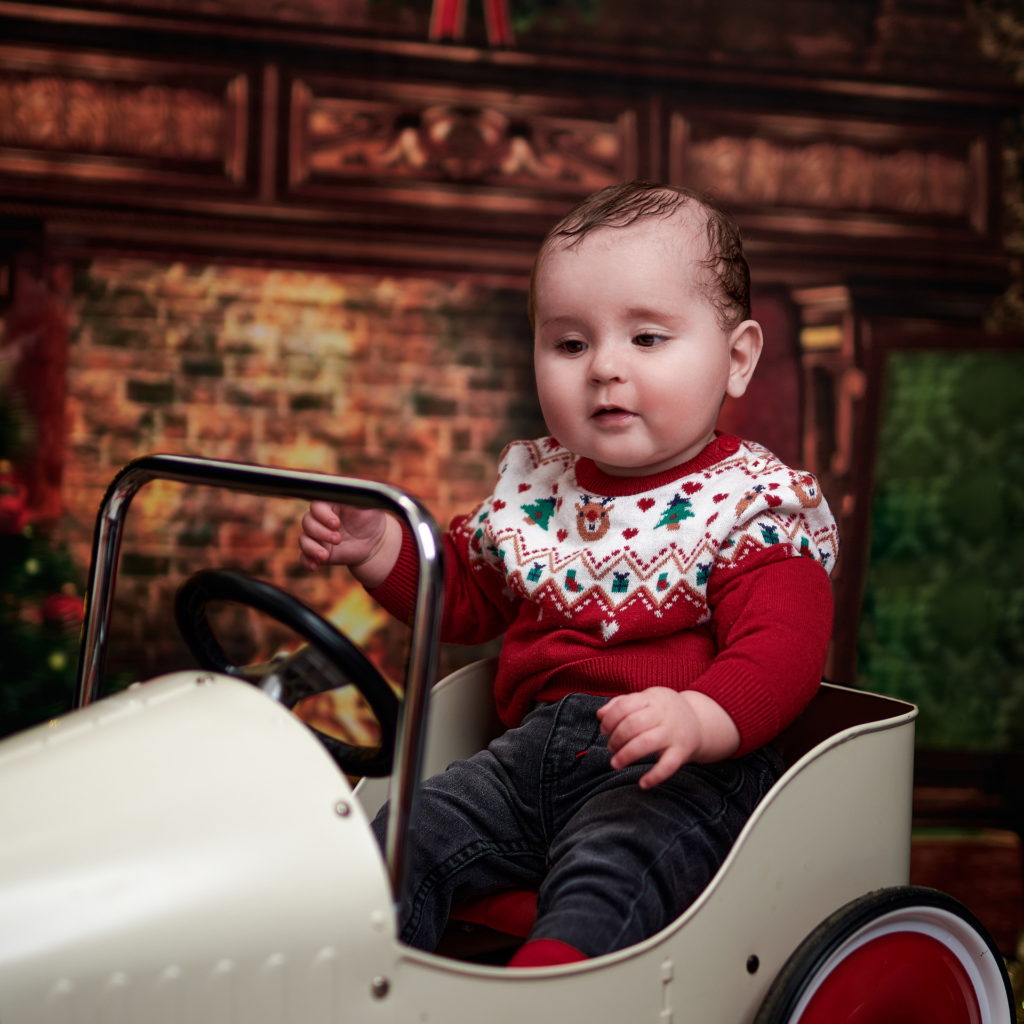 photo d'un bébé vêtu d'un pull de noël dans une voiture à pédale.