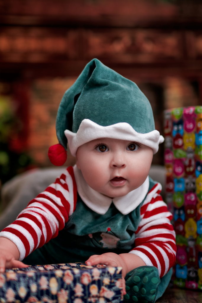 photo d'un bébé très mignon habillé en lutin ouvrant ses cadeaux à noël.