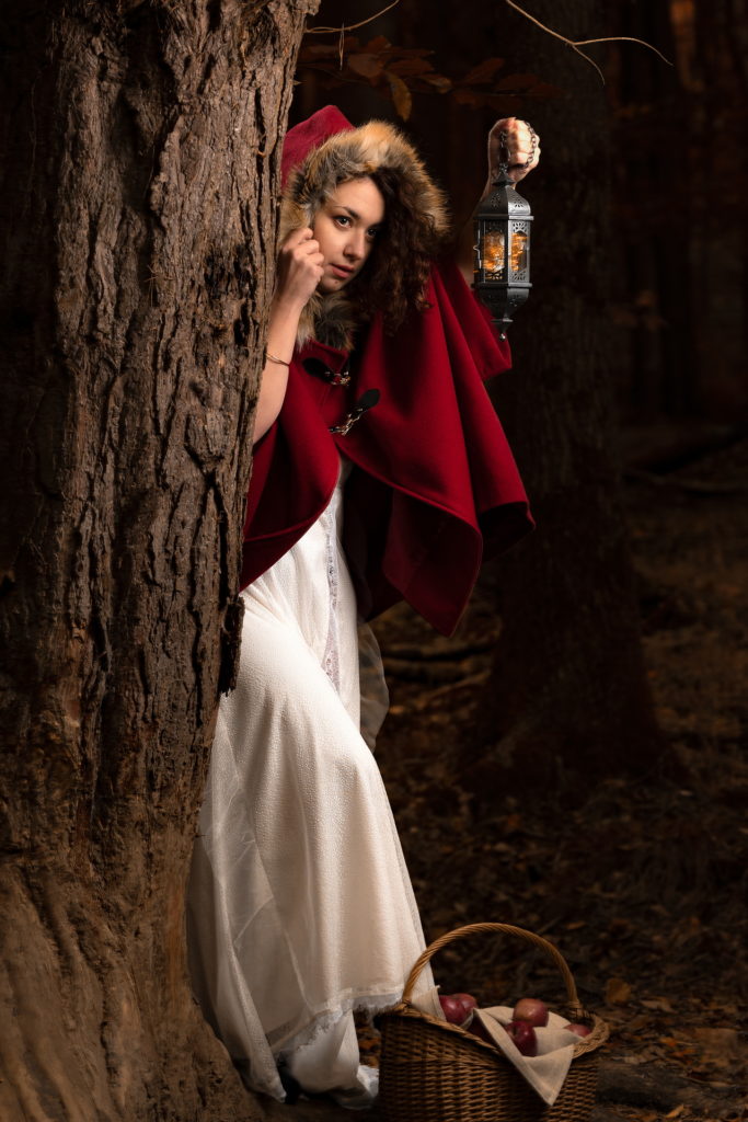 Femme habillée petit chaperon rouge se cache du loup derrière un tronc d'arbre avec une lanterne à la main