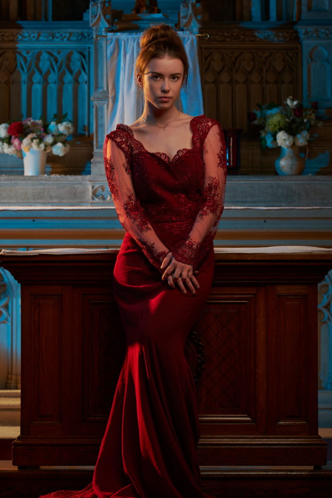 jeune femme vêtue d'une longue robe rouge à dentelle assise contre un hôtel dans une église à Rouen