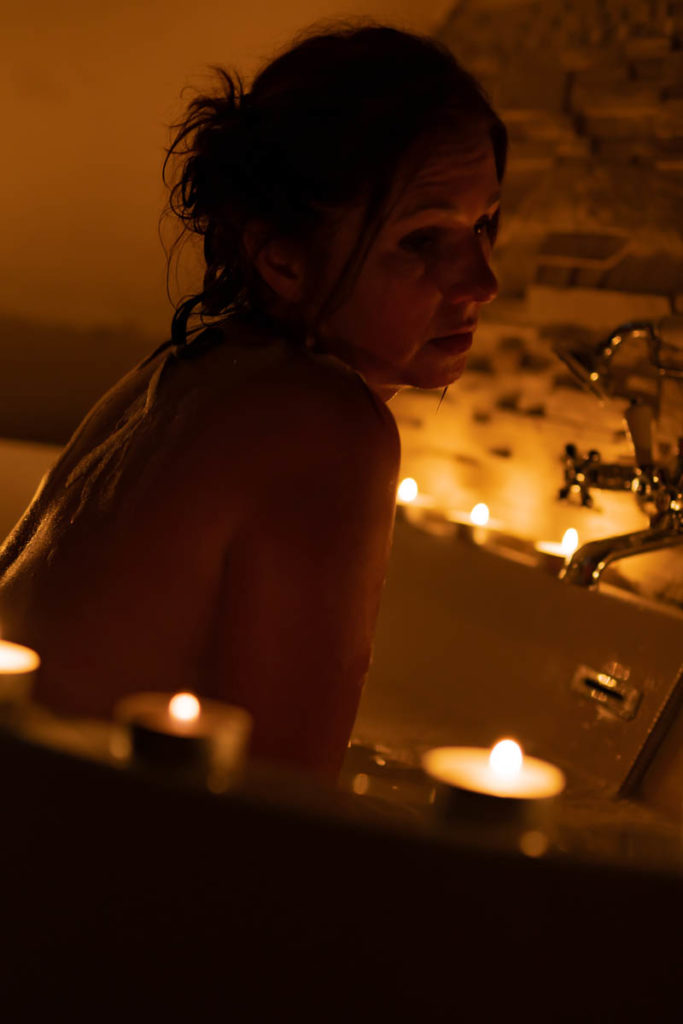femme nue dans un bain éclairée avec de nombreuses bougies posées au bord de la baignoire