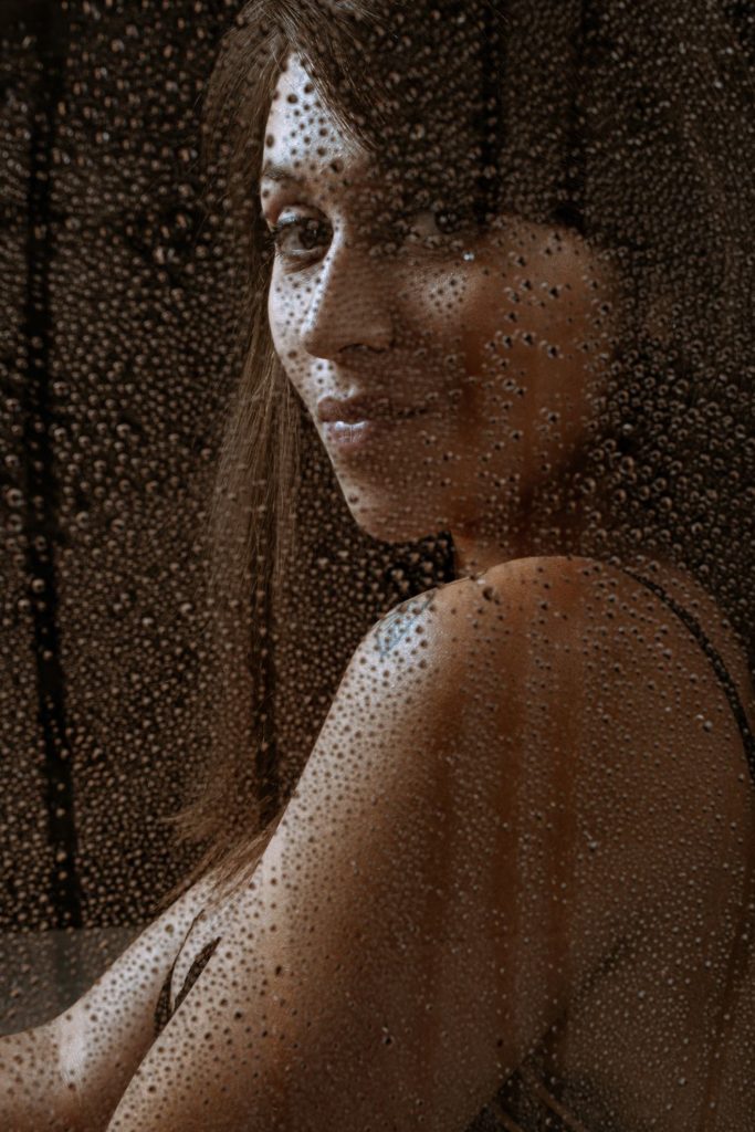 femme en lingerie derrière une vitre recouverte de gouttelettes d’eau
