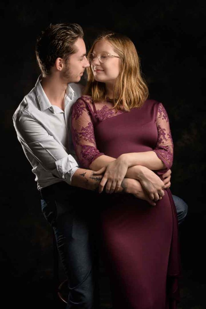 photo studio grossesse femme enceinte vêtue d'une robe bordeaux noire dans les bras de son mari