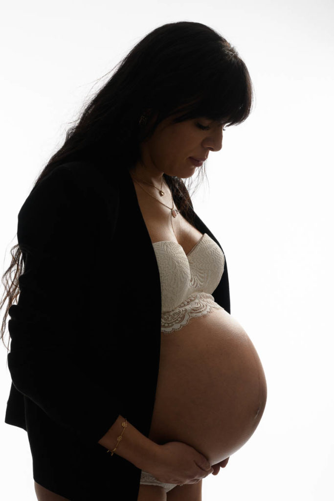 photo studio grossesse femme enceinte vêtue d'une veste noire devant fond blanc