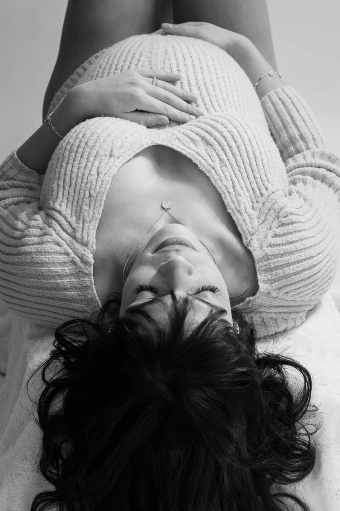 photo studio grossesse femme enceinte vêtue d'un pull allongée sur le dos en noir et blanc