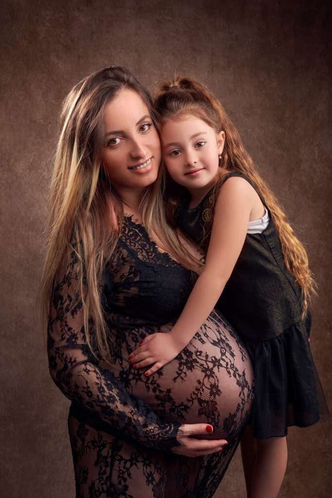 photo studio grossesse femme enceinte vêtue d'une robe en dentelle noire faisant un câlin à sa fille