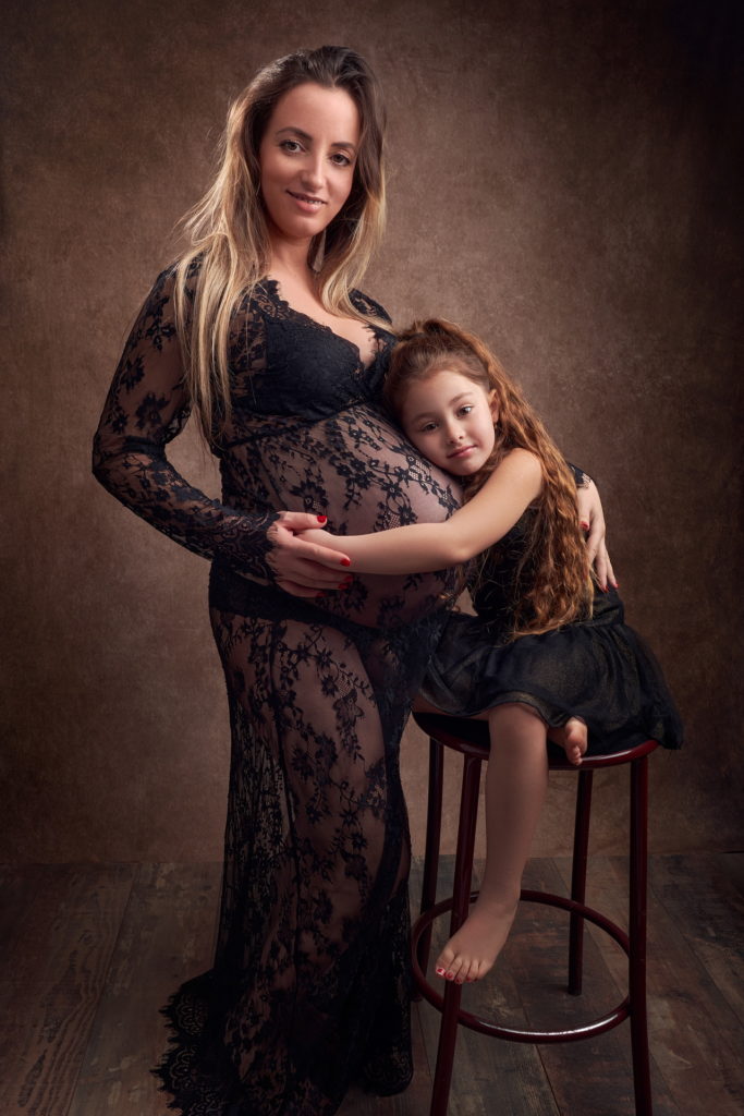 photo studio grossesse femme enceinte vêtue d'une robe en dentelle noire faisant un câlin à sa fille