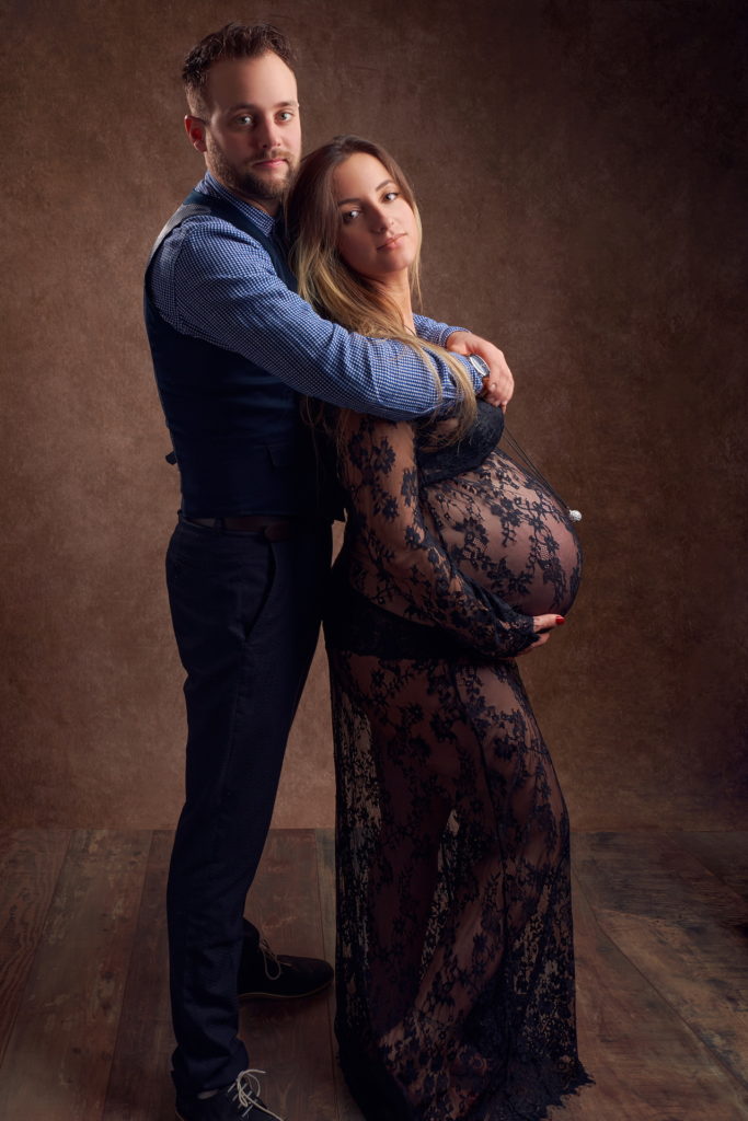 photo studio grossesse femme enceinte vêtue d'une robe en dentelle noire dans les bras de son mari