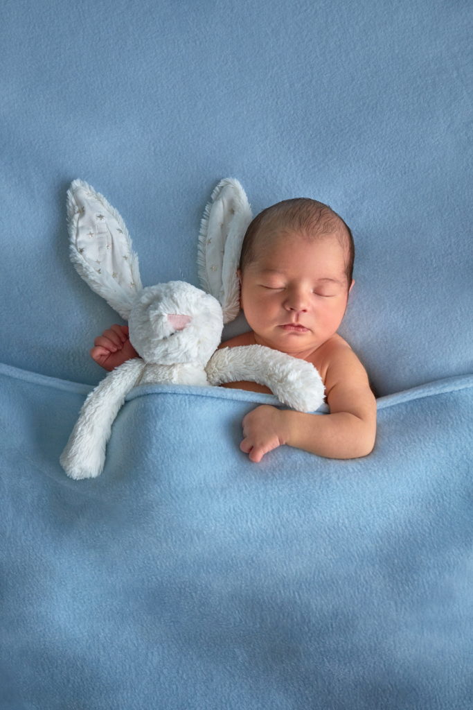 bébé endormi sous une couverture bleu tenant dans ses bras son doudou lapin blanc