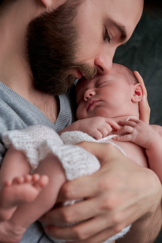 papa avec son bébé dans les bras, ils se font un câlin le bébé à son front sur la joue de son père.