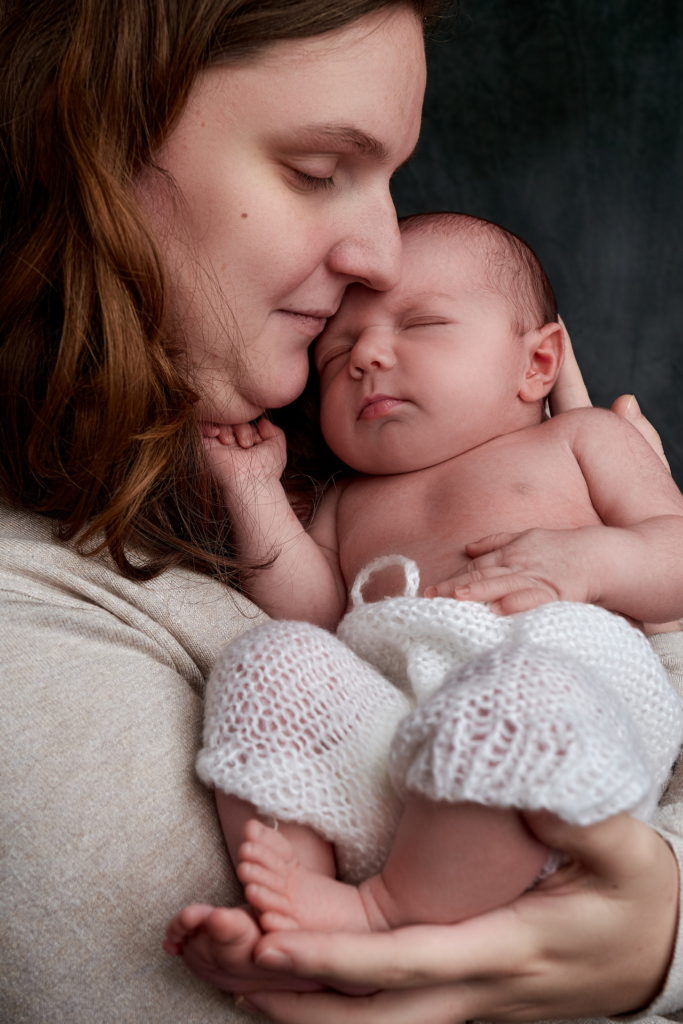 maman avec son bébé dans les bras, ils se font un câlin le bébé à son front sur la joue de sa mère.