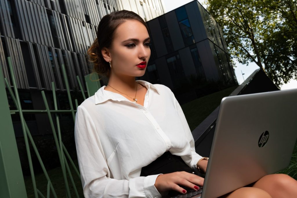 femme d'affaire à Rouen vêtue d'un tailleur et chemisier blanc très élégante, assise dehors travaillant sur son ordinateur