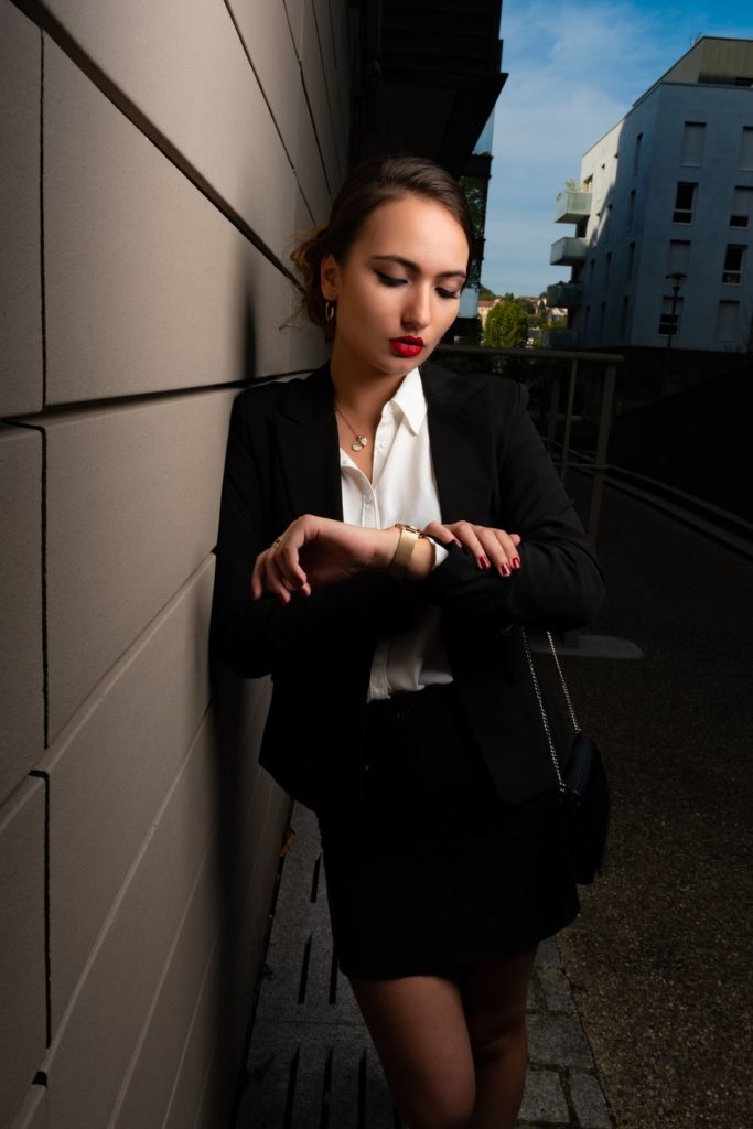 femme d'affaire à Rouen regardant sa montre vêtue d'un tailleur et veste noir très élégante.