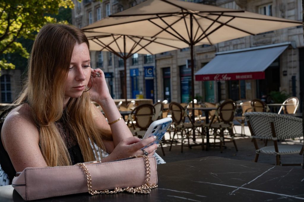 femme à la terrasse d'un café à bordeaux regardant son téléphone portable