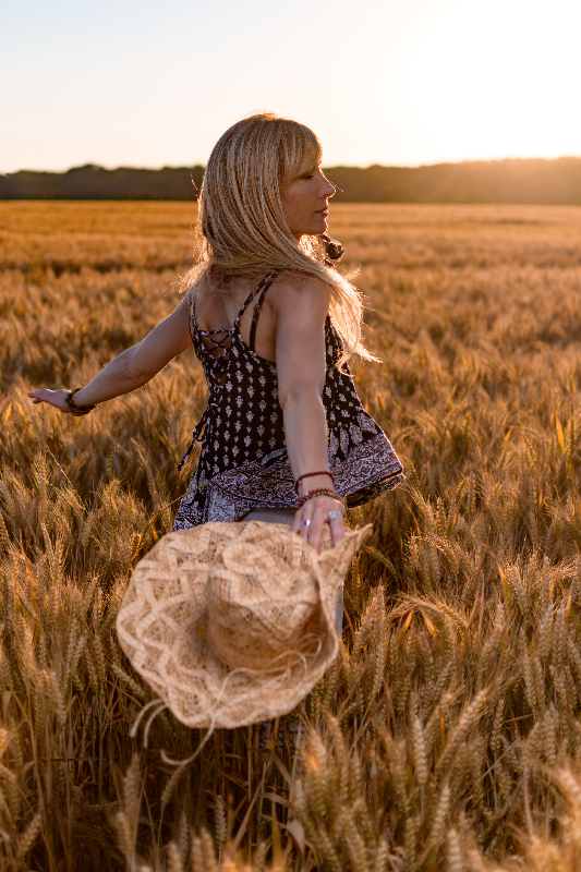 photo prise en coucher de soleil, femme blonde dansant dans un champ de blé un chapeau de paille à la main